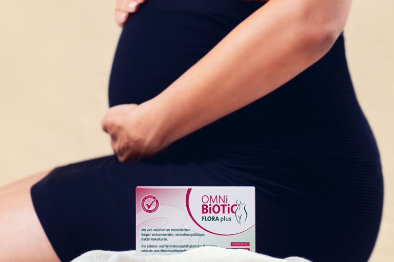 Bauch einer schwangeren Frau von der Seite mit OMNI BiOTiC Flora plus Verpackung zur Kamera