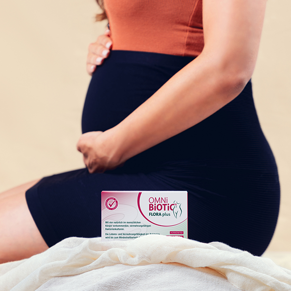 Bauch einer schwangeren Frau von der Seite mit OMNI BiOTiC Flora plus Verpackung zur Kamera